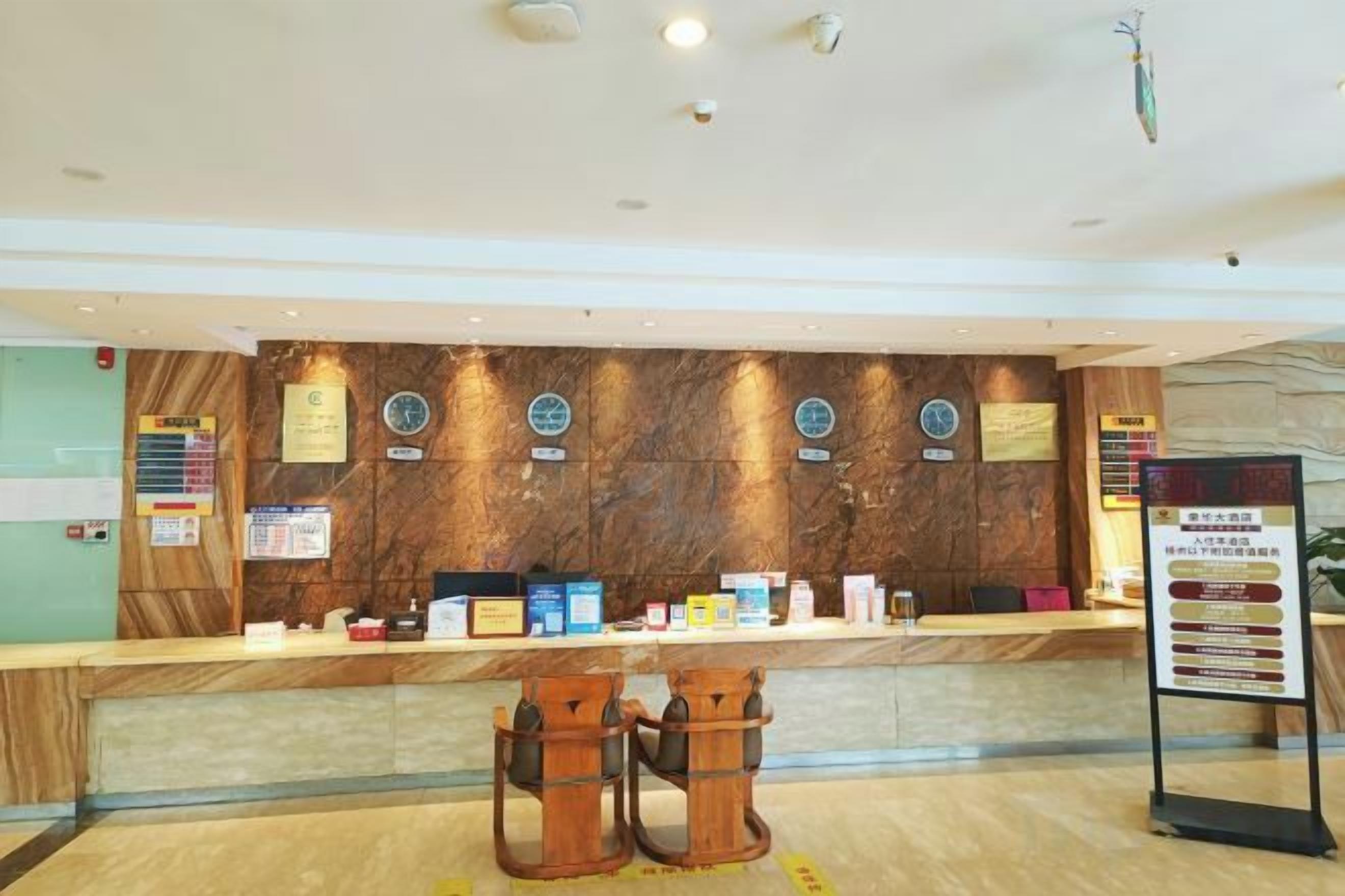 A hotel reception area with a marble reception desk, two wooden chairs, and a bulletin board with information.