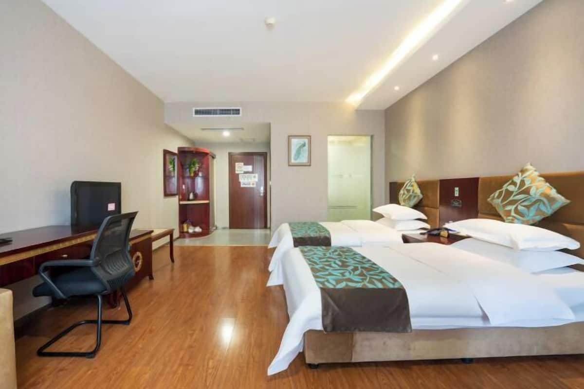 A hotel room with a desk, two beds, a chair, and a door.