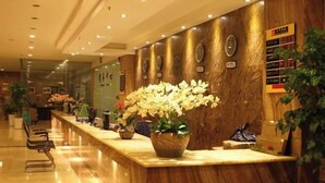 Zona de recepción de hotel con mostrador de mármol, plantas en macetas, un reloj de pared y un tablón de directorio.
