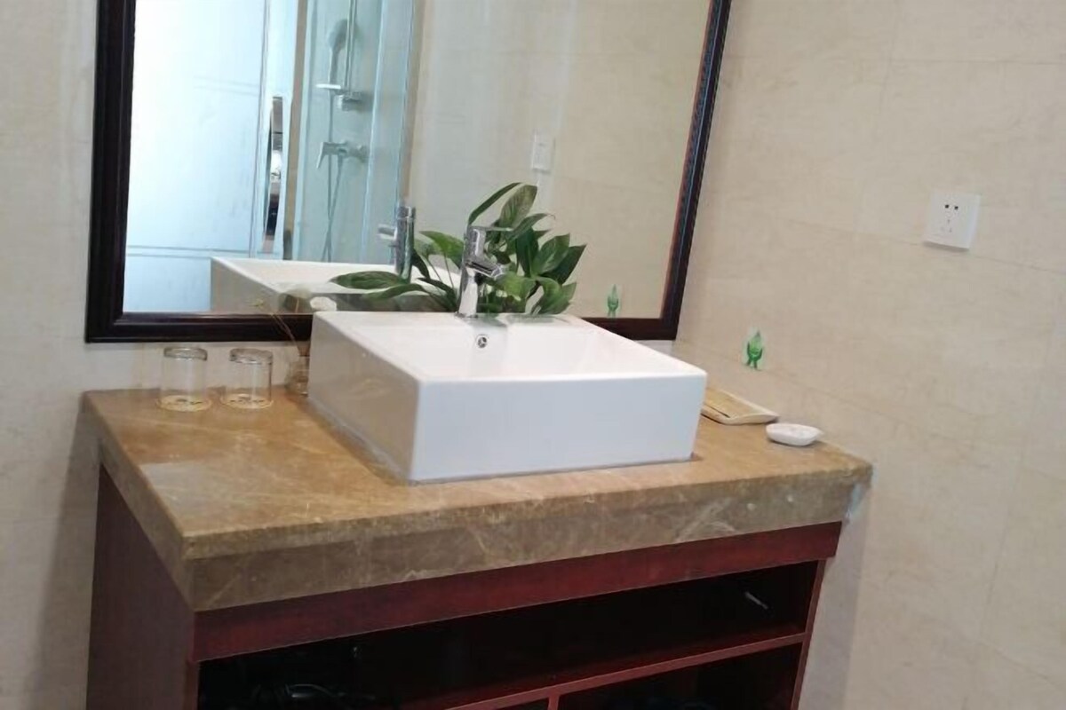 A bathroom with a white rectangular sink, a mirror, and a plant on the countertop.