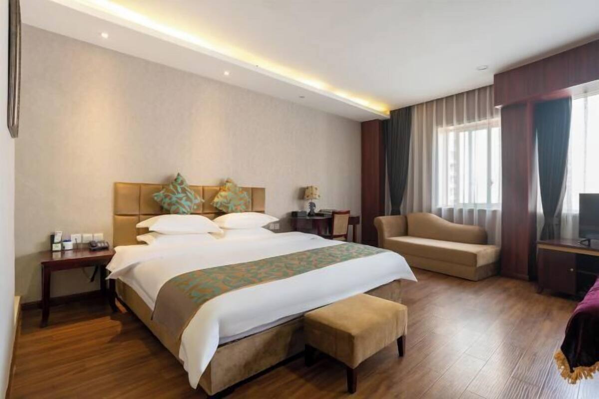 A hotel room with a large bed, a sofa, a desk, and a TV.