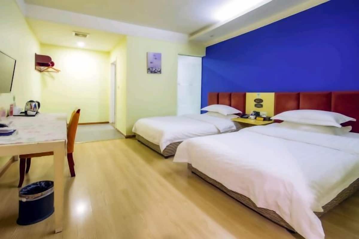A hotel room with two beds, a desk with a chair, a small table, and a trash bin.