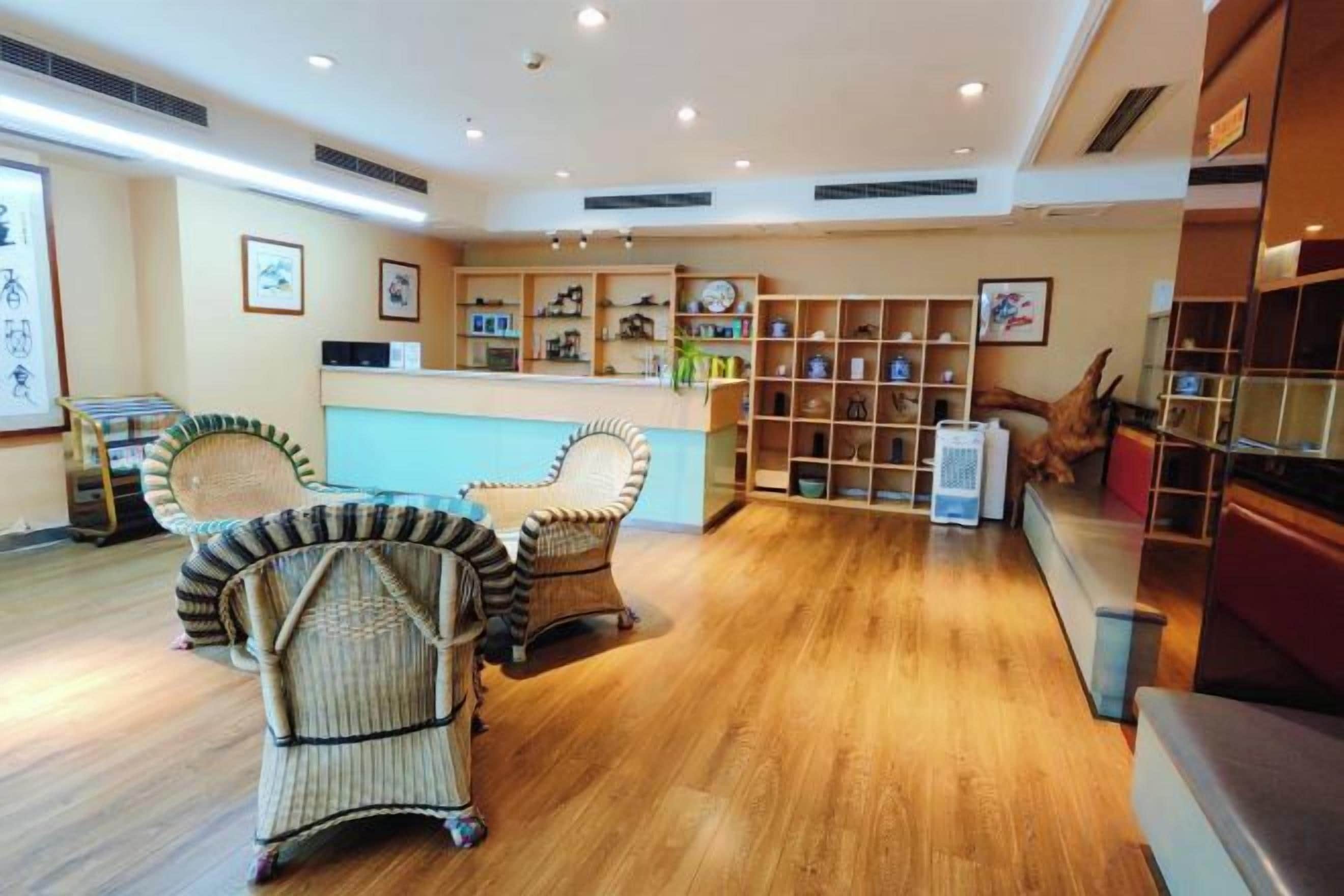 A hotel lobby with a reception desk, wicker chairs, wooden flooring, and a bookshelf.