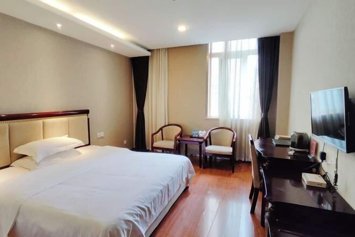 A hotel room with a bed, a desk, a chair, a television, and a window with curtains.