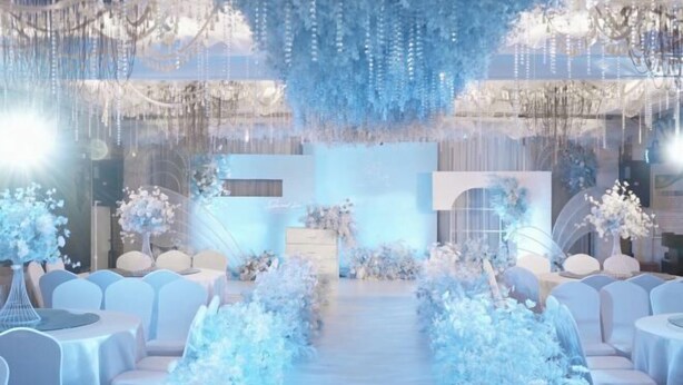 Un salón de bodas con un pasillo central, sillas blancas y decoración floral.