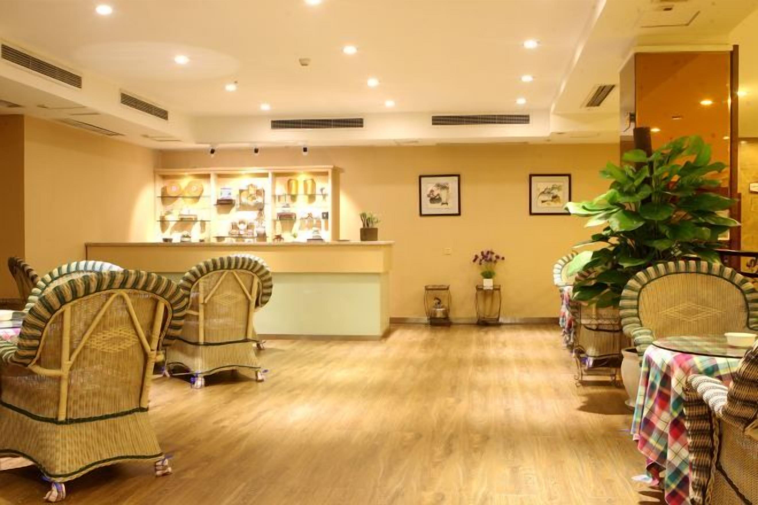 A hotel lobby with wicker chairs, a reception desk, and a large potted plant.