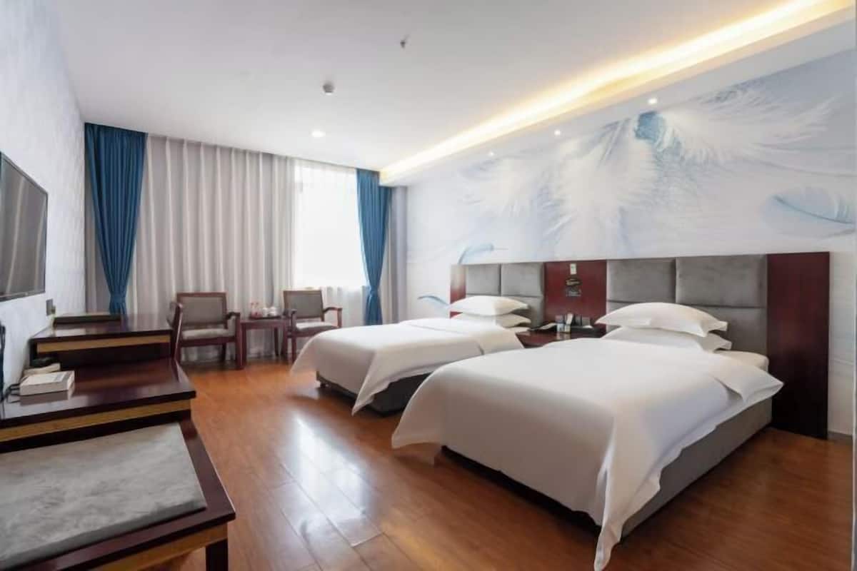A hotel room with two beds, a desk, a chair, and a large window with curtains.