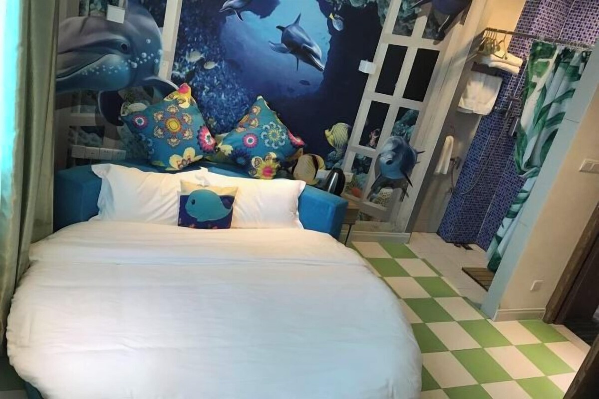 Un dormitorio con cama, almohadas coloridas, un mural de delfines, suelo a cuadros y zona de ducha.