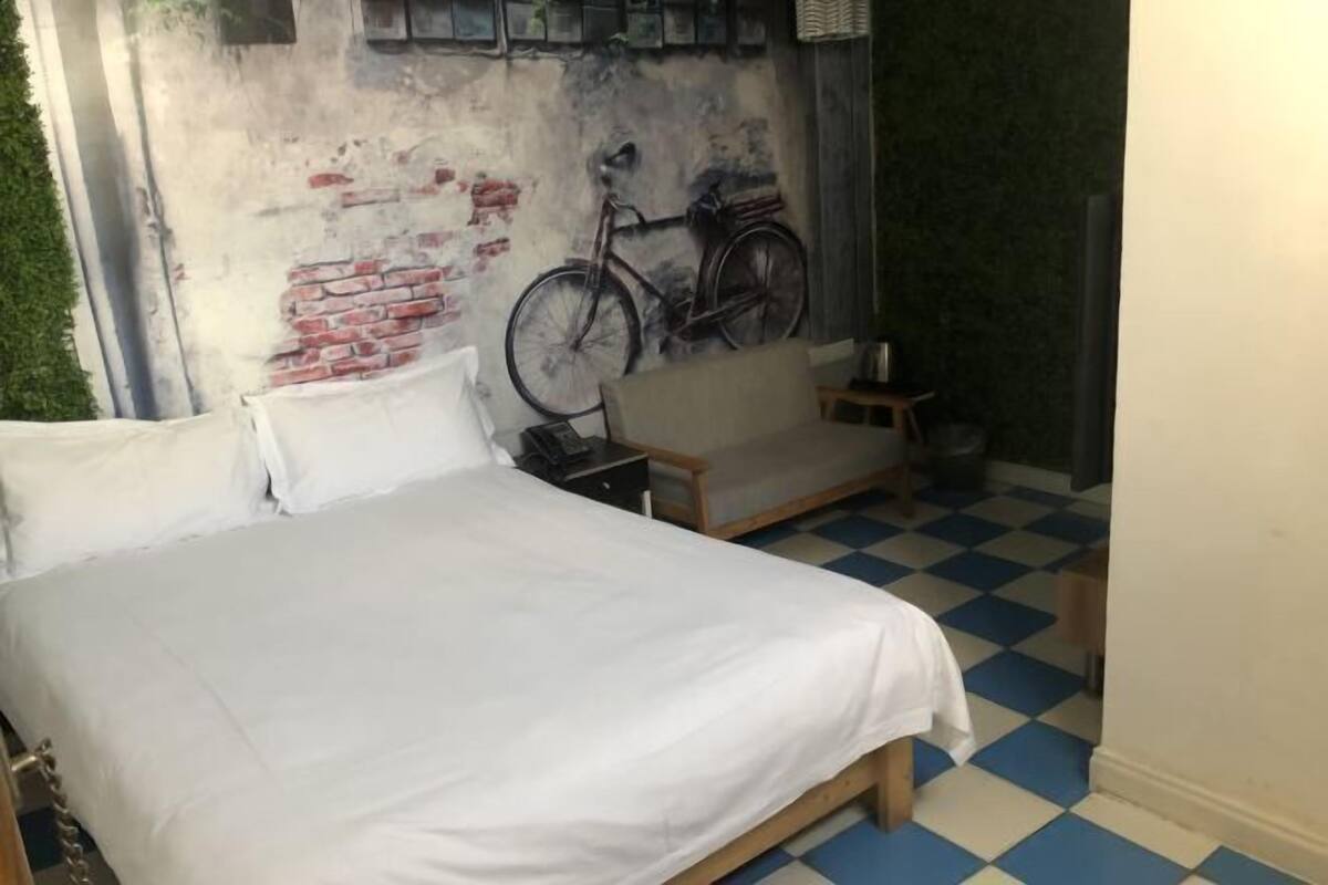 Una habitación con cama, una mesita, una silla y un mural en la pared de una bicicleta.