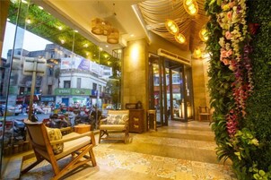 Un vestíbulo de hotel con asientos, una recepción, una pared verde con flores y vistas a la calle.