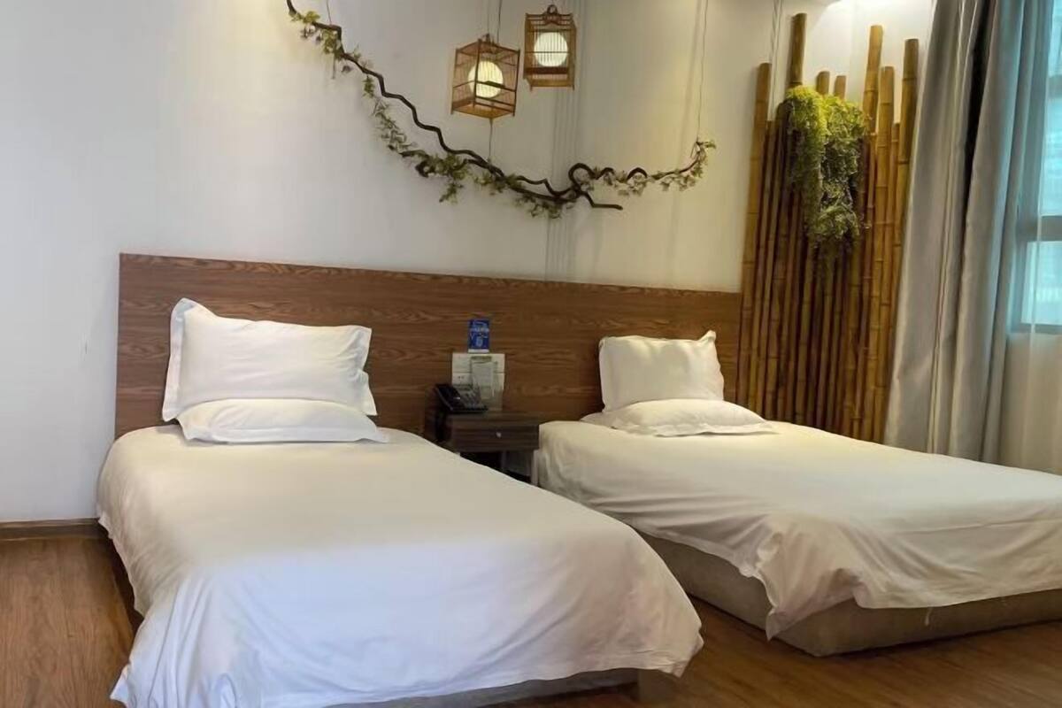 Una habitación de hotel con dos camas, un cabecero de madera, una mesita de noche con un teléfono y una pared decorativa con una enredadera y faroles.
