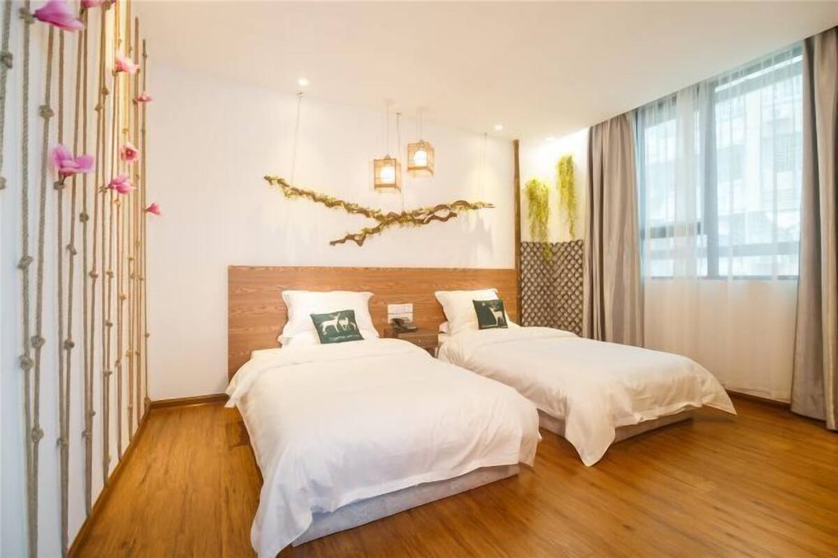 Habitación de hotel con dos camas, suelo de madera, pared decorativa y un ventanal grande.