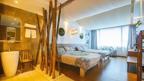 Une chambre d’hôtel avec un grand lit, un coin salon avec un fauteuil, une grande fenêtre et une salle de bain avec un lavabo et un miroir.