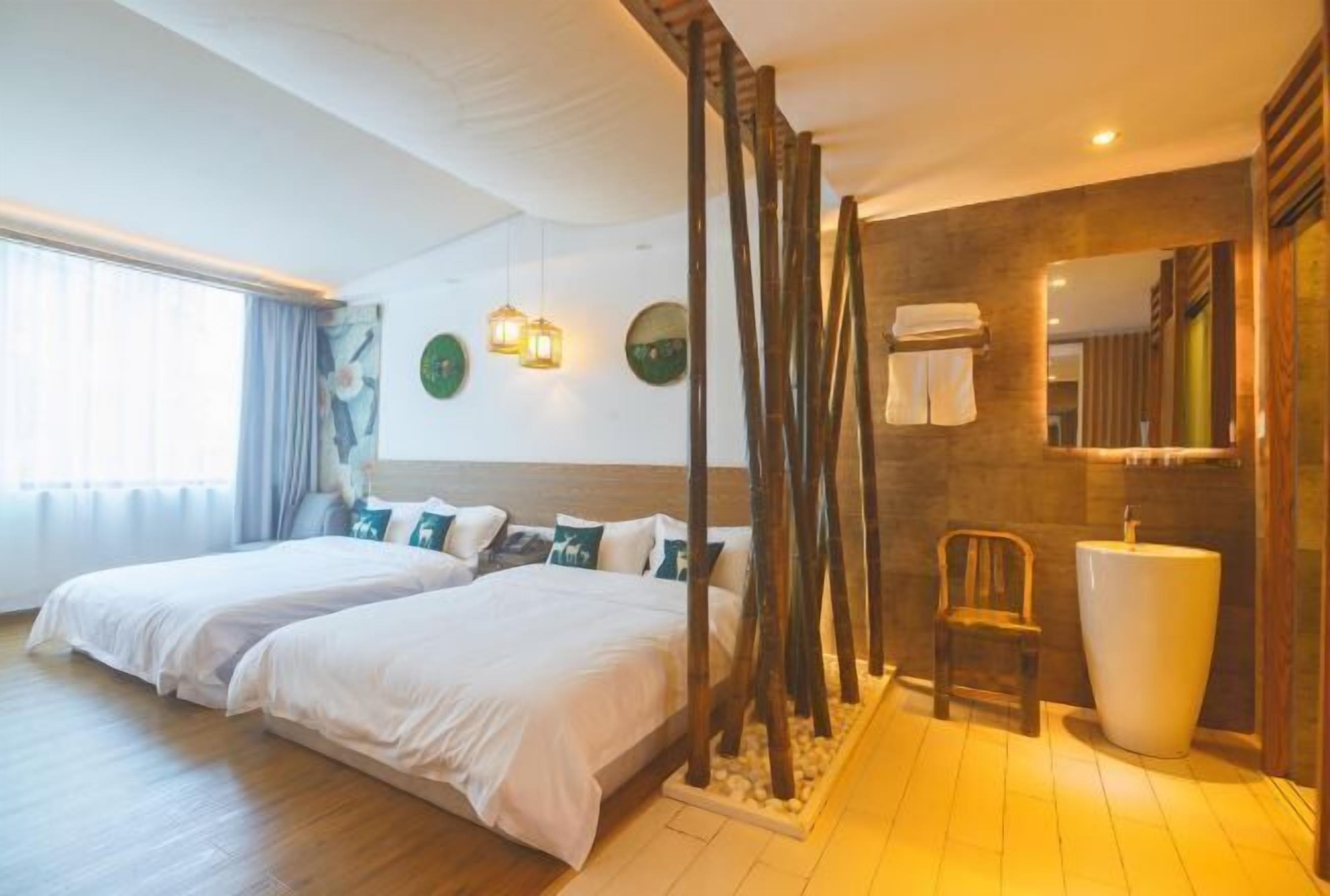 A hotel room with two beds, a wooden floor, a large mirror, a white sink, and a chair.