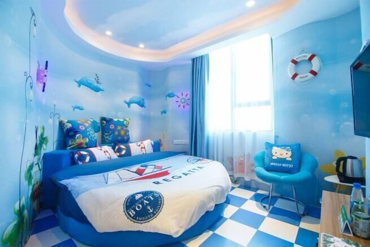Una habitación con piso a cuadros, una cama con cubrecama de temática náutica, un sillón azul y un adorno de salvavidas en la pared.