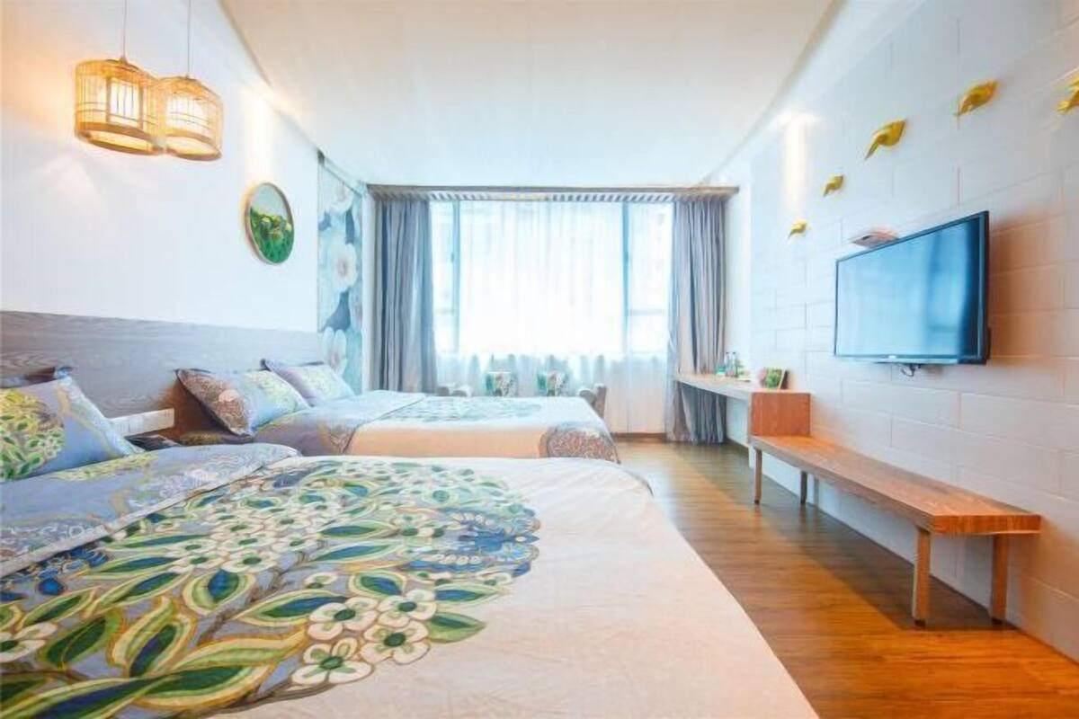 Habitación de hotel con dos camas, televisión, un banco y una ventana con cortinas.