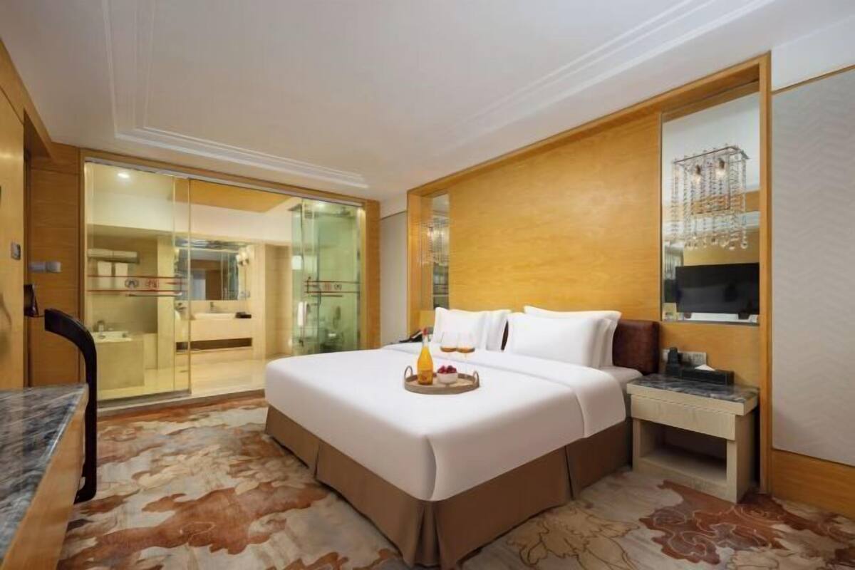 Une chambre d’hôtel dotée d’un grand lit, d’un bureau avec une chaise, d’une salle de bain fermée par des parois de verre et d’un mur décoratif en bois.
