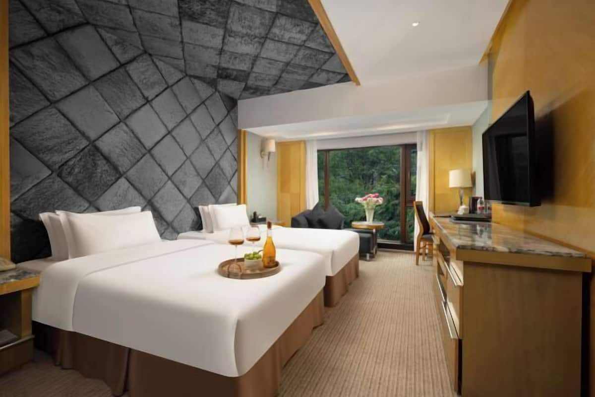 Une chambre d’hôtel avec un grand lit, un bureau, une télévision et une vue sur la verdure environnante.