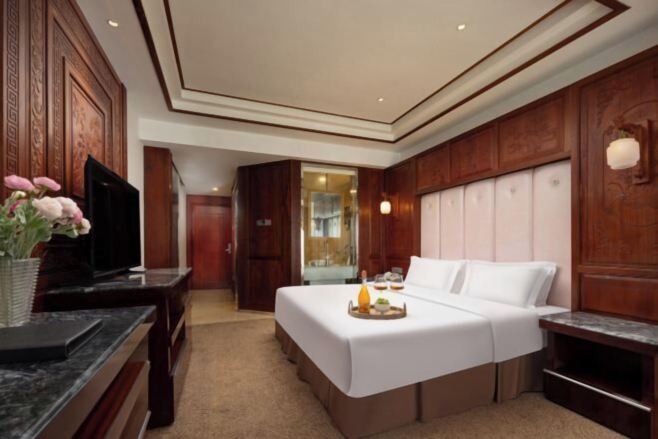 A hotel room with a large bed, a desk with a television, and a bathroom visible through an open door.