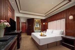 Habitación de hotel con una cama grande, un escritorio con televisor y un baño visible a través de una puerta abierta.
