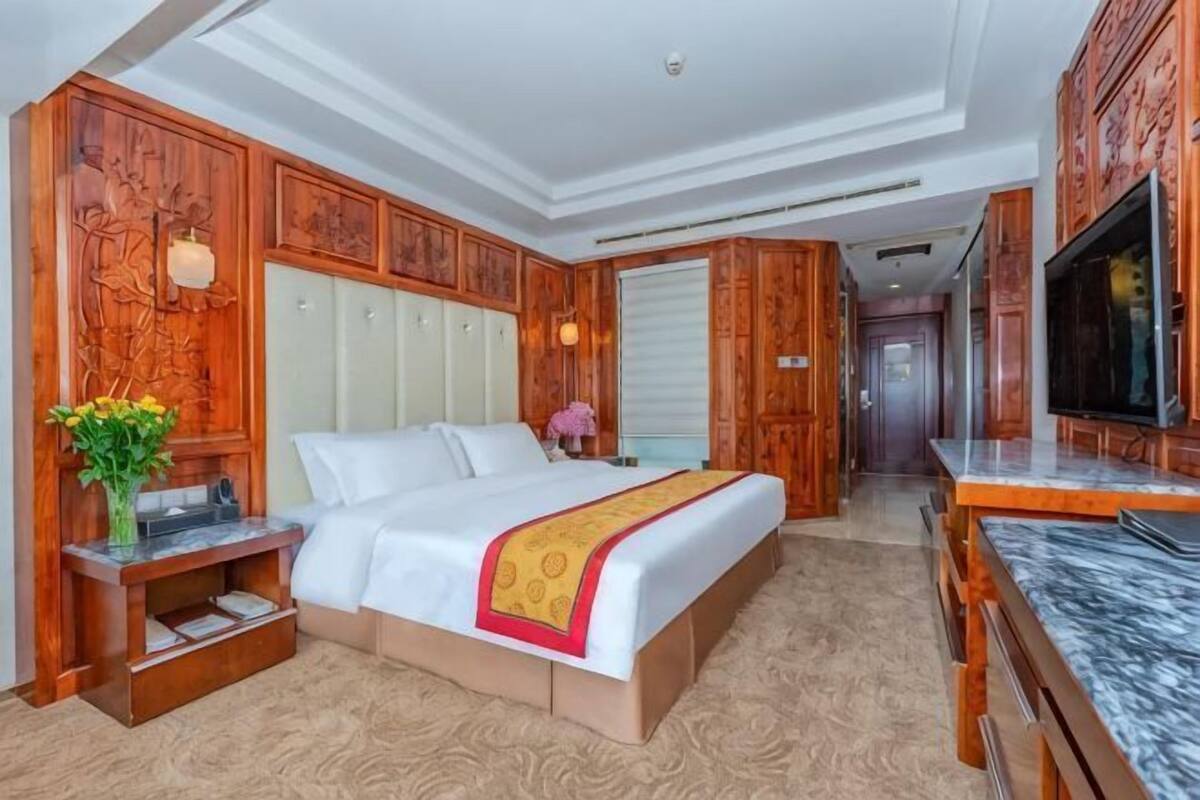 Une chambre d’hôtel avec un grand lit, des boiseries, une télévision et un comptoir en marbre.