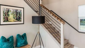 Un escalier avec une main courante en bois et des balustres en métal, un lampadaire noir et un tableau représentant un paysage, encadré, accroché au mur.