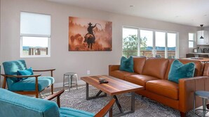 Un salon moderne avec un grand tableau représentant un cow-boy, un canapé en cuir et une table basse en bois.