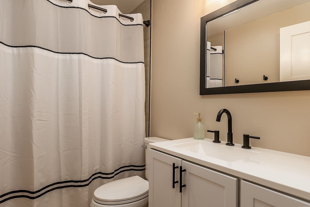 A bathroom with a white toilet, a white sink with a black faucet, and a mirror above the sink.