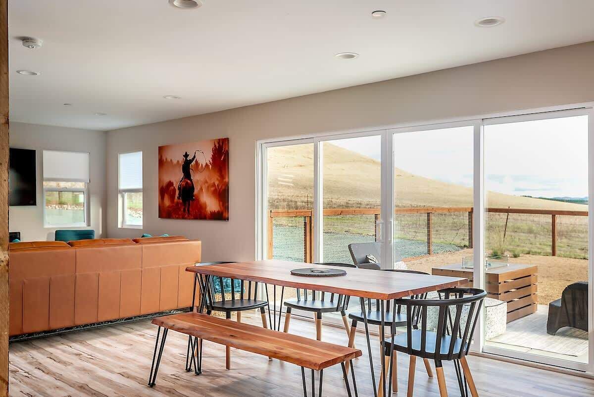 Une cuisine moderne avec une table et des chaises en bois, une grande fenêtre donnant sur un paysage désertique et un coin salon avec un canapé.