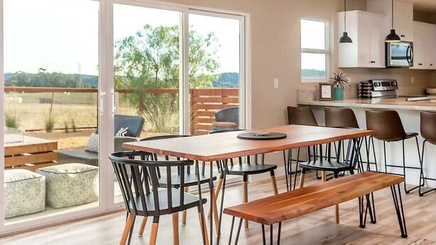 Une cuisine moderne dotée d’un grand îlot central, de portes-fenêtres coulissantes donnant sur un patio, et d’un coin repas avec une table et des chaises en bois.