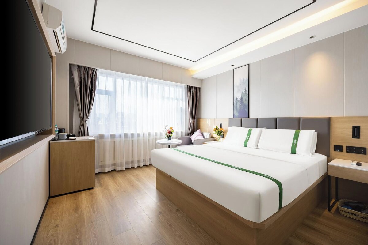 Moderni hotellihuone, jossa on suuri sänky, yöpöytä, työpöytä ja litteänäyttöinen televisio.