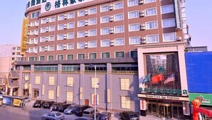 Un hôtel à plusieurs étages, avec une rangée de fenêtres à chaque niveau, une enseigne indiquant « Green Tree Inn Express » et un parking où sont garées plusieurs voitures.
