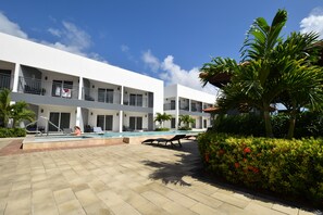 Een modern hotel met een zwembad, meerdere balkons en weelderige begroeiing.