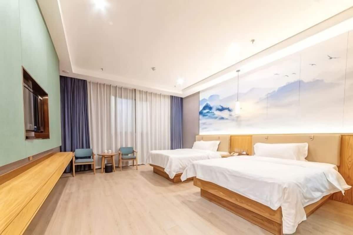 A hotel room with two beds, a desk, a chair, and a large window with curtains.
