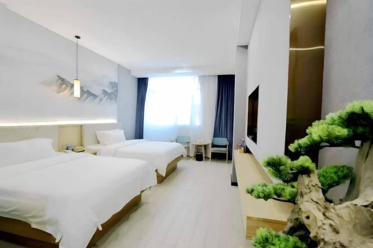 A hotel room with two beds, a desk, a chair, a TV, and a decorative tree.