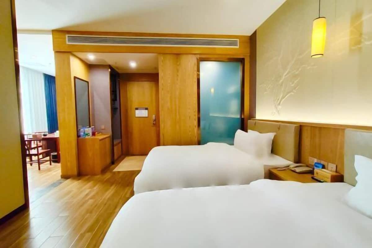 A hotel room with two beds, a desk, a chair, and a wall-mounted lamp.