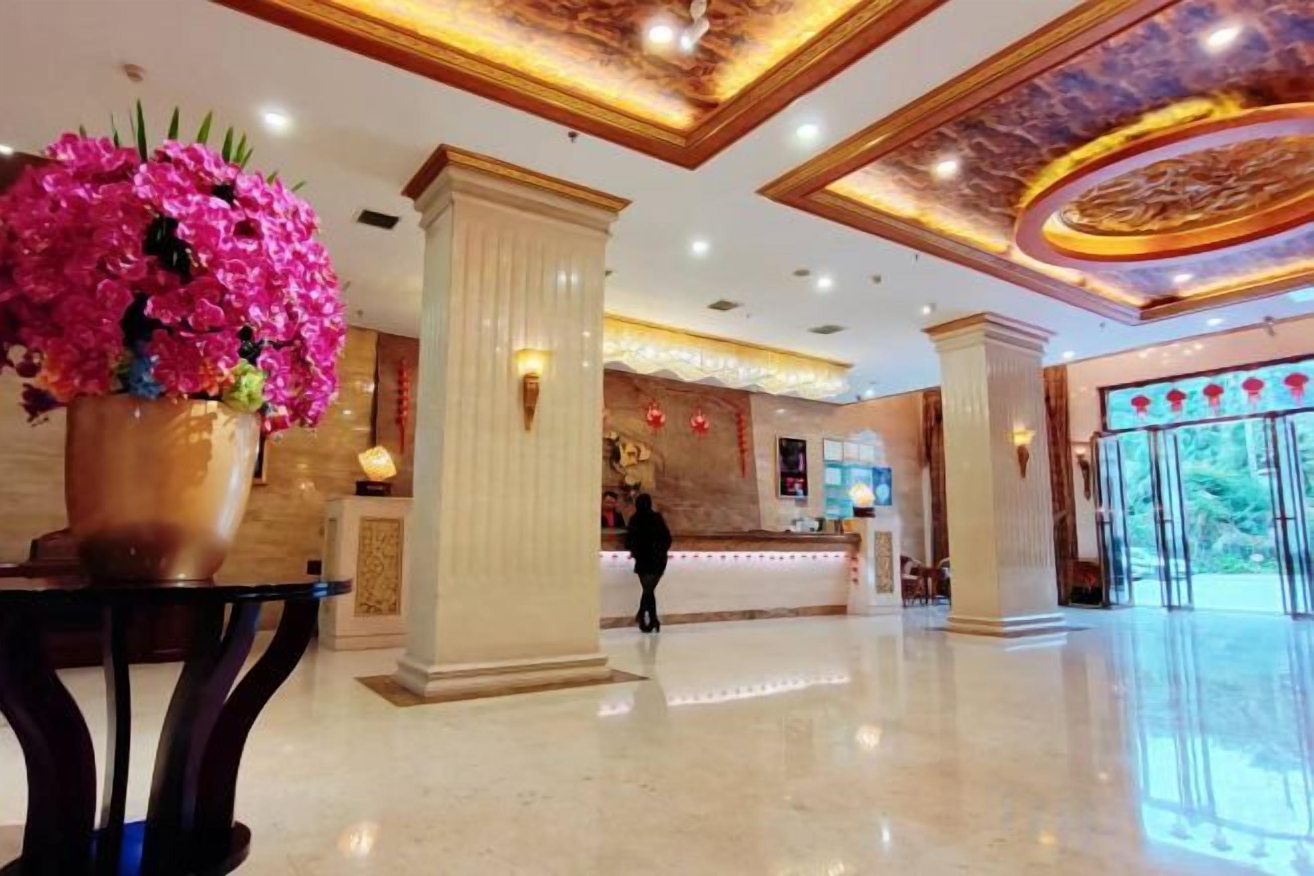 A hotel lobby with a reception desk, a large floral arrangement, and a polished marble floor.