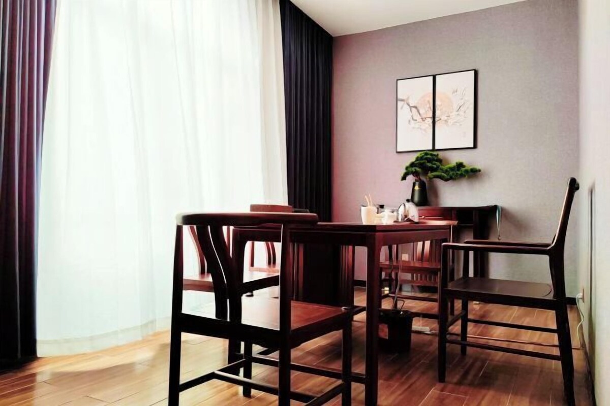 A dining area with a table and chairs, a potted plant, and a wall-mounted artwork.