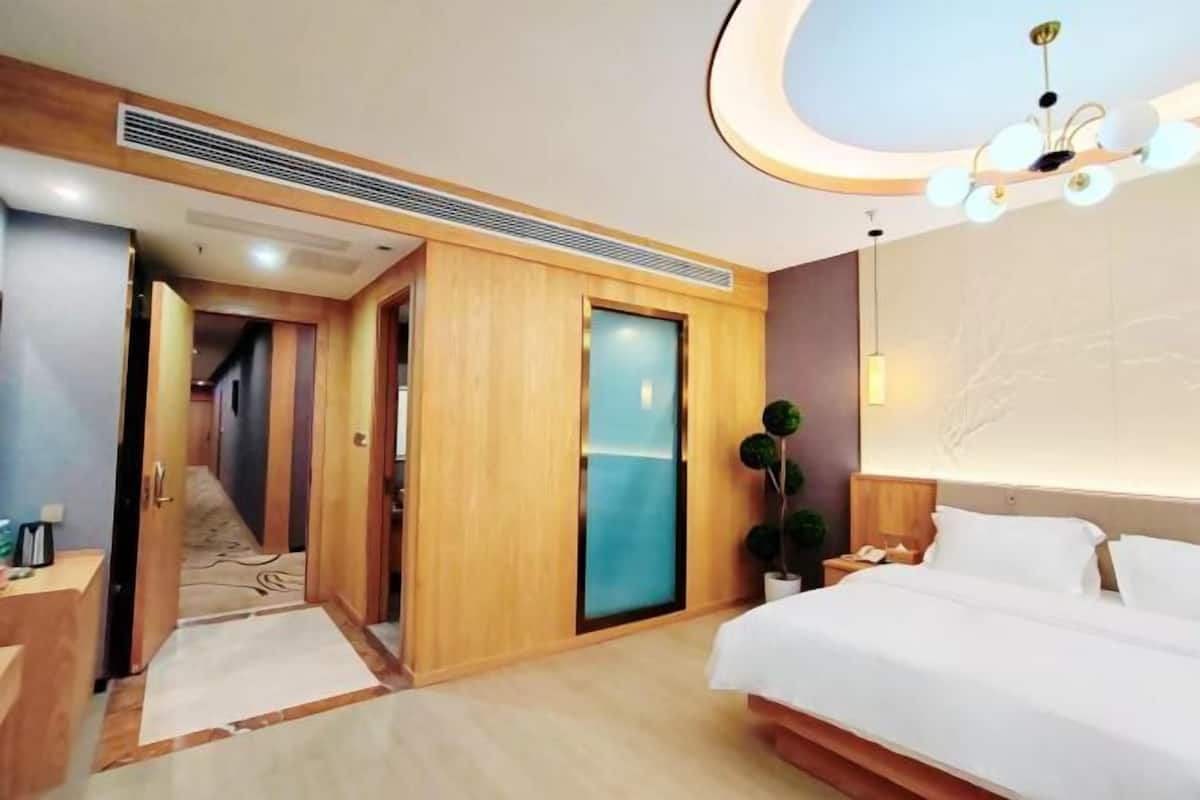 A hotel room with a bed, bedside table, lamp, and a view of the hallway.