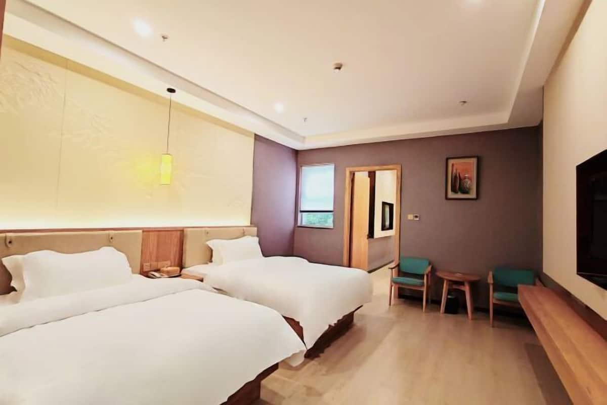 A hotel room with two beds, a desk, a chair, and a TV.