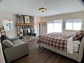 A bedroom with a stone fireplace, a bed with plaid bedding, a gray armchair, and a wooden ladder. - Ideally Located, Sun Valley Chalet (Ketchum)