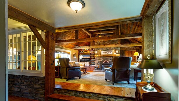 Un intérieur rustique avec des poutres en bois, des murs en pierre et un coin salon confortable agrémenté de fauteuils et d’une cheminée.