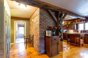 Cozy kitchen with exposed beams, brick accent wall, and wooden cabinet, leading to a dining area with a wooden table and chairs.