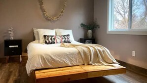Una camera da letto con un letto, un comodino, una finestra e una decorazione appesa al muro.