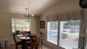 Comedor con mesa y sillas de madera, una araña y ventanas grandes con persianas.