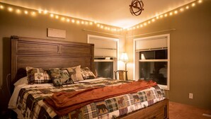 Un dormitorio con cabecera de madera, colcha acolchada, manta roja y luces de cadena.