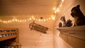 Interior acogedor de una cabaña con una cama nido de madera, una estantería con piñas y luces colgantes.