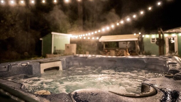 Un jacuzzi con una manguera, rodeado de una atmósfera brumosa y luces de cuerda al fondo.
