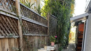 A narrow garden path with a wooden fence, potted plants, and a flamingo sculpture. - Cute Tropical Beach Studio Walk to Ocean and All! (Long Beach)