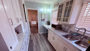 A modern kitchen with a built-in microwave, double sink, and wooden cabinets. - Cute Tropical Beach Studio Walk to Ocean and All! (Long Beach)